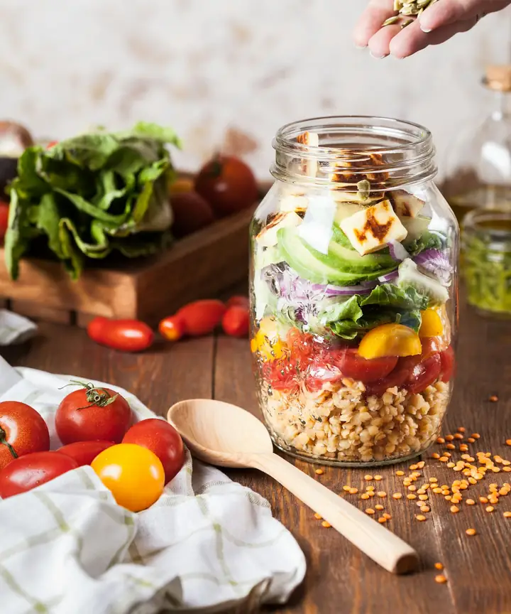 Layered salad in a glass jar beside fresh tomatoes